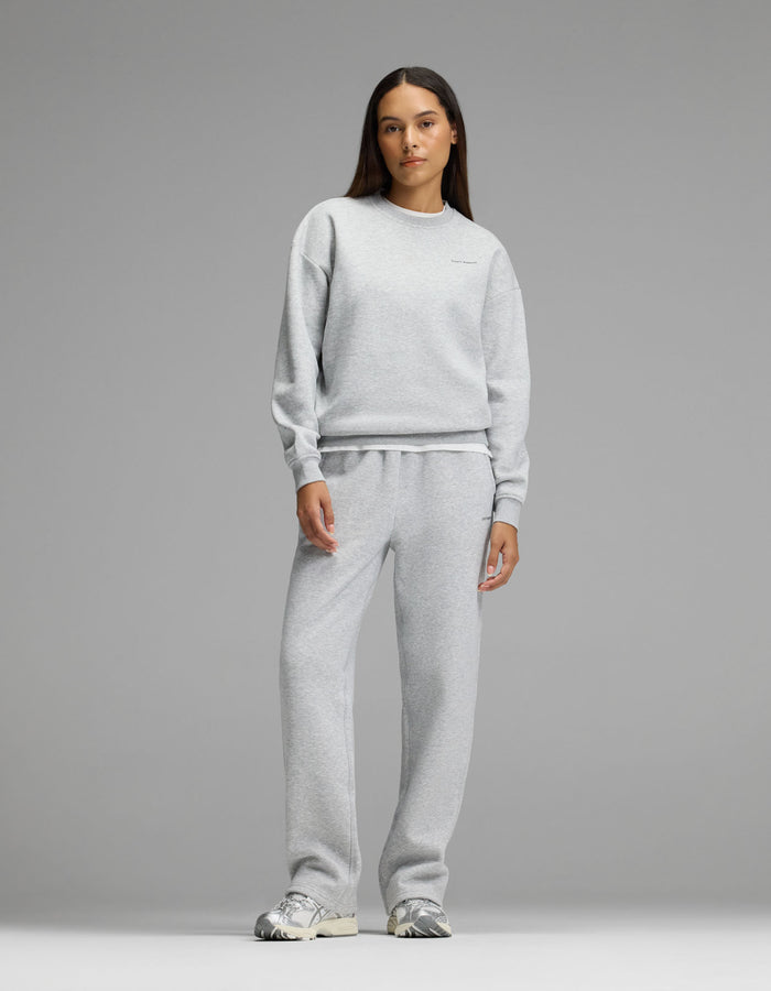 A woman stands facing forward against a plain gray background, wearing Cozy Earth’s Women’s Cityscape Crewneck & Wide Leg Pant Set in Heather Grey, paired with silver sneakers.|Color:Heather Grey