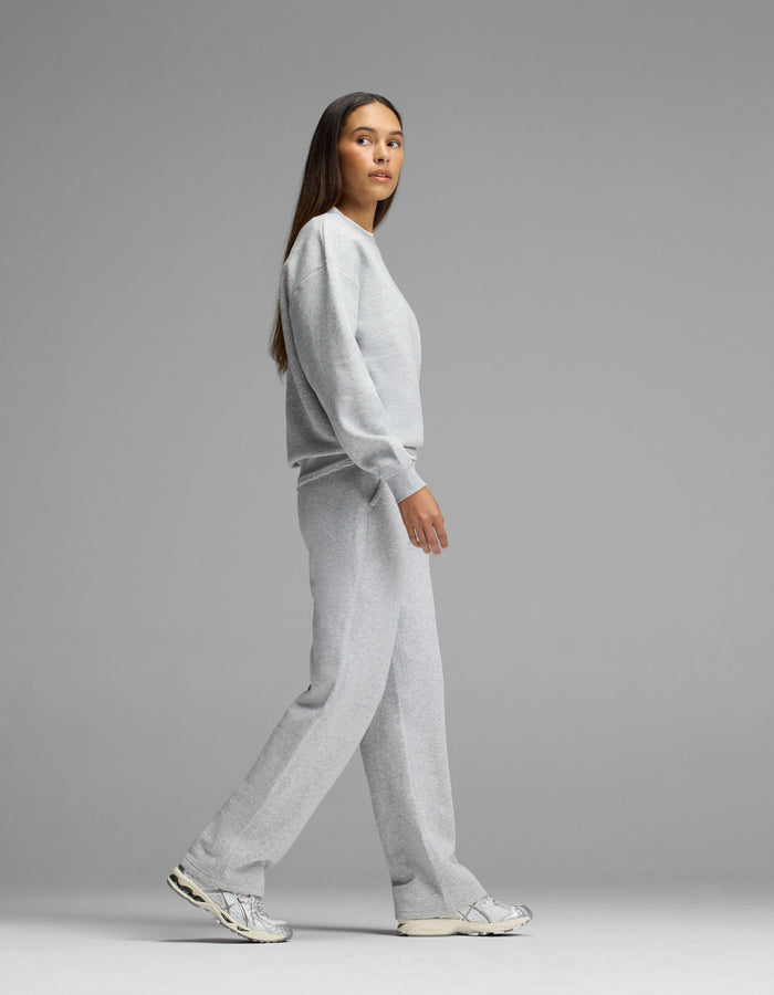 A person wearing the Cozy Earth Women’s Cityscape Crewneck & Wide Leg Pant Set walks to the left against a plain gray background, paired with white sneakers.|Color:Heather Grey
