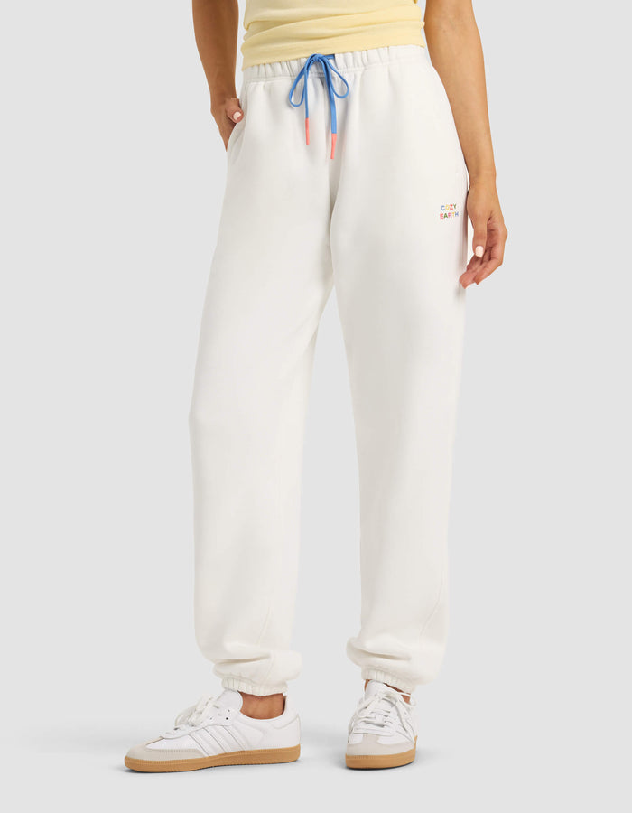 A person models Cozy Earth's Women's Cityscape Sweatpant in white, paired with a yellow top and white sneakers, hands in pockets, against a plain background. |Color:Sea Salt