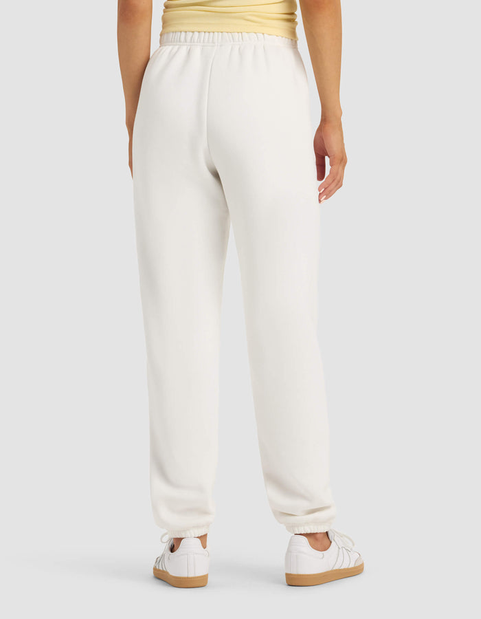 A person is seen from behind wearing the Cozy Earth Women's Cityscape Sweatpant in white, paired with a light yellow top and white sneakers, standing against a plain light gray background.|Color:Sea Salt