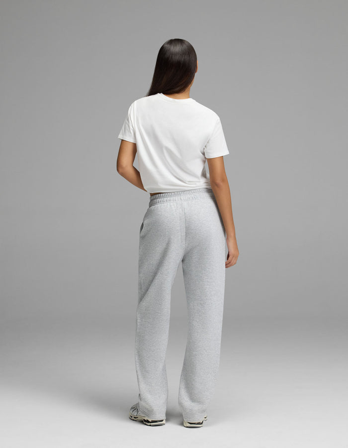 A person with long dark hair stands facing away, wearing a white t-shirt, Cozy Earth Women’s Cityscape Wide Leg Pant in light gray, and white sneakers against a plain gray background.|Color:Heather Grey