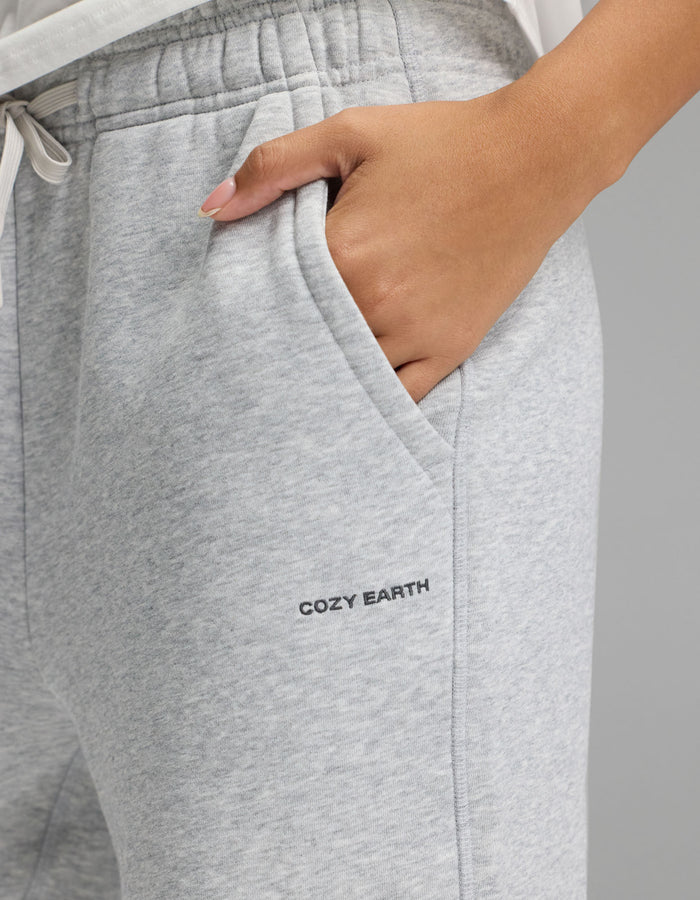 A person wearing the Cozy Earth Women’s Cityscape Wide Leg Pant in light gray, with a hand in the pocket and “COZY EARTH” printed near the pocket.|Color:Heather Grey