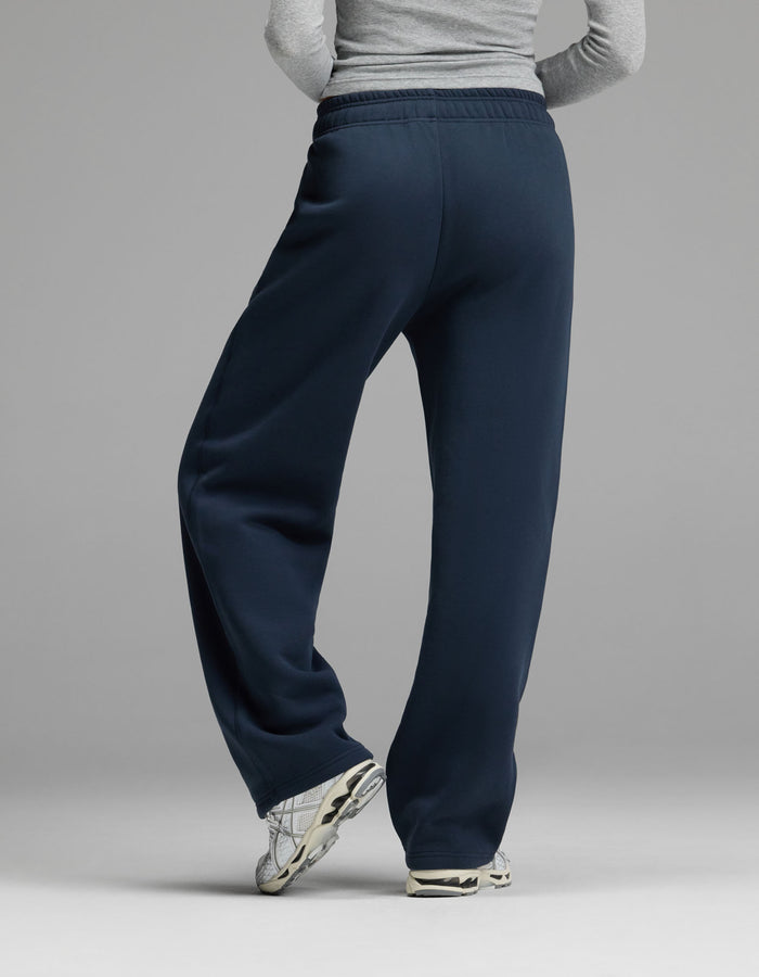 A person wearing a gray long-sleeve shirt, Cozy Earth Women’s Cityscape Wide Leg Pant in navy blue, and white sneakers stands with legs crossed, facing away from the camera against a plain gray background.|Color:Eclipse