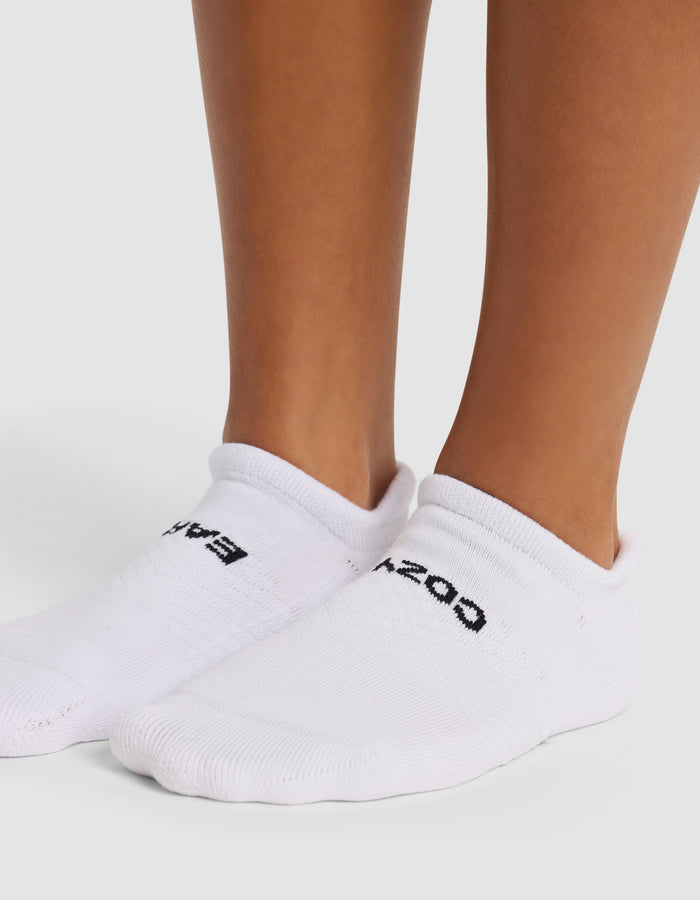 A close-up of two feet wearing Cozy Earth Essential Ankle Sock, white and low-cut with black text on top, standing on a light surface.|Color:White
