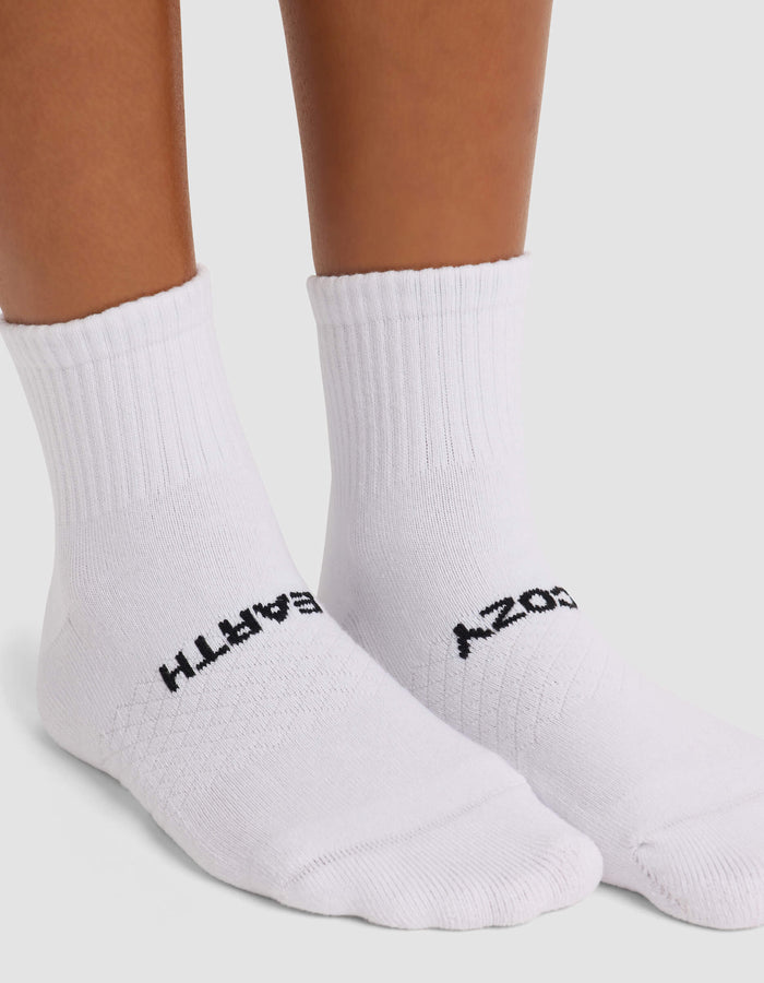 A person wears Cozy Earth's Women's Essential Quarter Socks—white with black text, "EARTH" on the left and "COZY" on the right. The socks feature ribbed tops and are shown against a plain white background.|Color:White