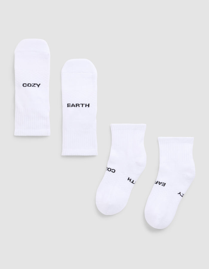 Four white Essential Quarter Socks from Cozy Earth are laid flat on a light gray background. Each features black text: one pair reads “COZY” and “EARTH,” while the other’s text shows parts of “EARTH,” “COZY,”.  |Color:White