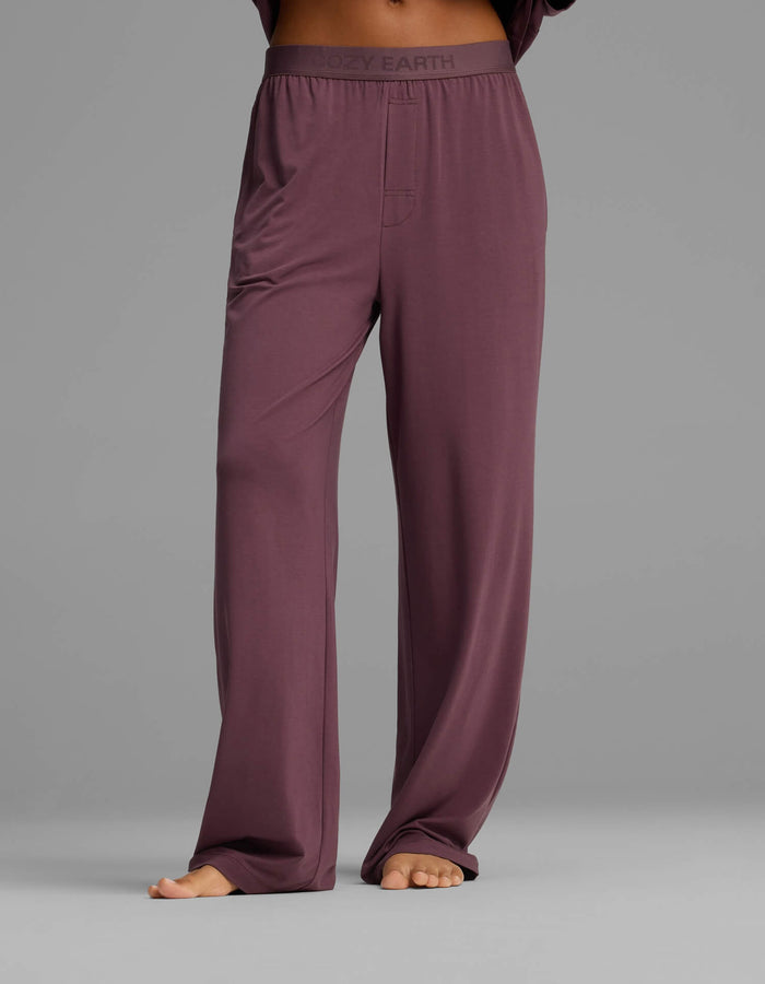 A person is barefoot against a plain gray background, wearing Cozy Earth’s Women’s First Layer Pajama Short Sleeve Tee & Pant Set, featuring loose-fitting, high-waisted mauve pants with an elastic waistband.|Color:Fig