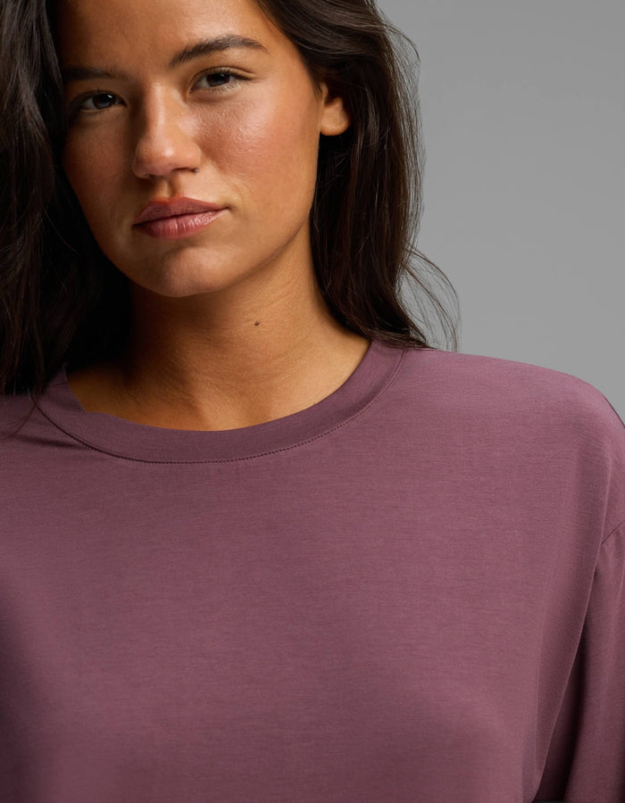 A woman with long dark hair, wearing the Cozy Earth Women’s First Layer Long Sleeve Sleep Tee in mauve, stands against a plain background, looking directly at the camera with a neutral expression.|Color:Fig