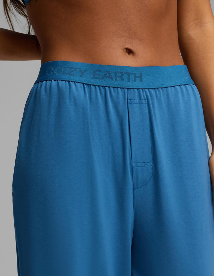 A close-up shows the lower torso and part of one arm of a person wearing the Cozy Earth Women’s First Layer Pajama Short Sleeve Tee & Pant Set in blue, with “COZY EARTH” visible on the waistband.|Color:Anchor