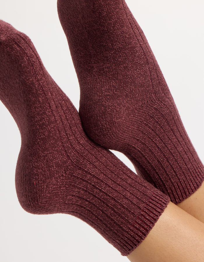 A pair of feet wear Cozy Earth's Plush Lounge Quarter Socks in burgundy, featuring a cozy ribbed knit and textured pattern, shown against a plain light background.|Color:Burgundy/Tulip/Blossom