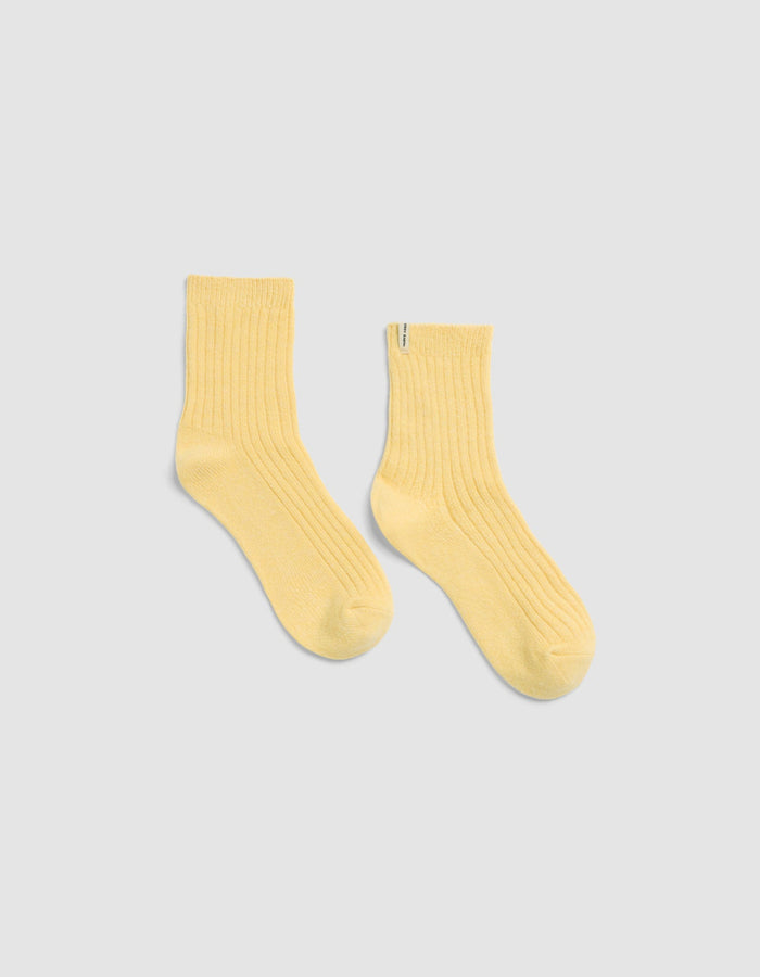 The Plush Lounge Quarter Socks by Cozy Earth in light yellow, featuring a ribbed crew design, is displayed laid flat on a light gray background.|Color:Daisy