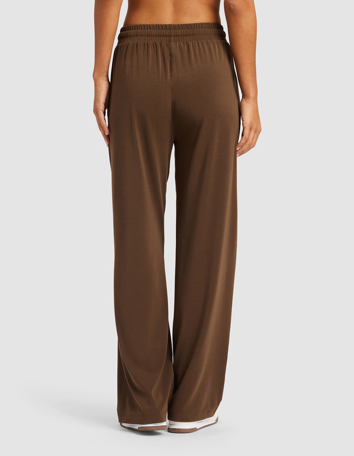 A woman is shown from the back, barefoot on a white background, wearing Cozy Earth’s Women's Studio Wide Leg Pant in brown with a loose fit and elastic waistband.|Color:Espresso