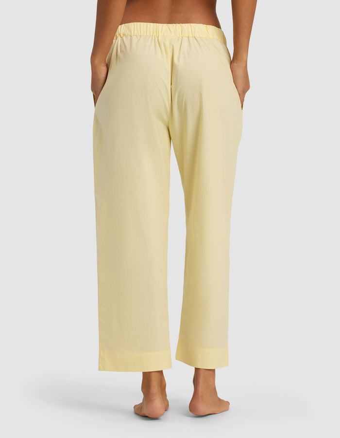 A person stands barefoot, facing away from the camera, wearing Cozy Earth's Women's Sutton Cropped Pajama Pant in light yellow with an elastic waistband and hands in the side pockets.|Color:Meringue