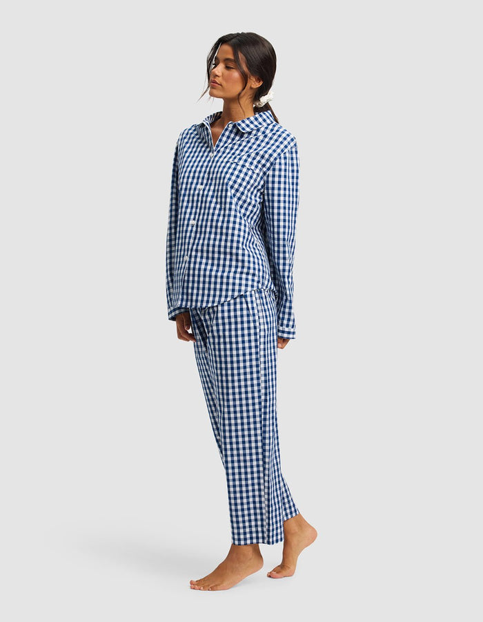 A woman stands barefoot against a light grey background, wearing the Cozy Earth Women's Sutton Long Sleeve Pajama Set in blue and white checkered print.|Color:Pacific Gingham
