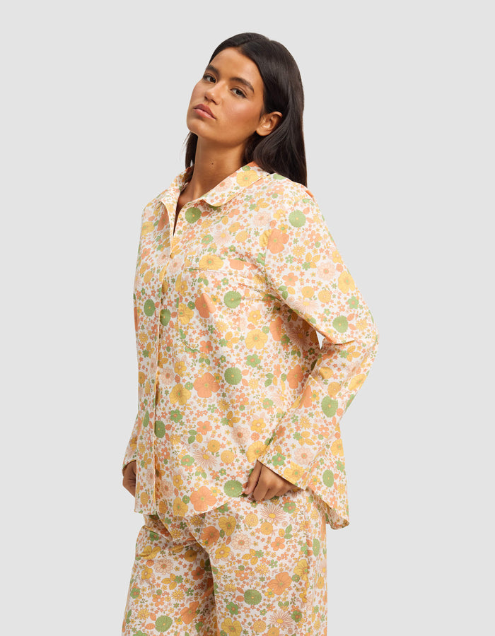A woman with long dark hair wears the Cozy Earth Women's Sutton Long Sleeve Pajama Top, featuring a colorful floral pattern, against a plain light gray background.|Color:Wildflower