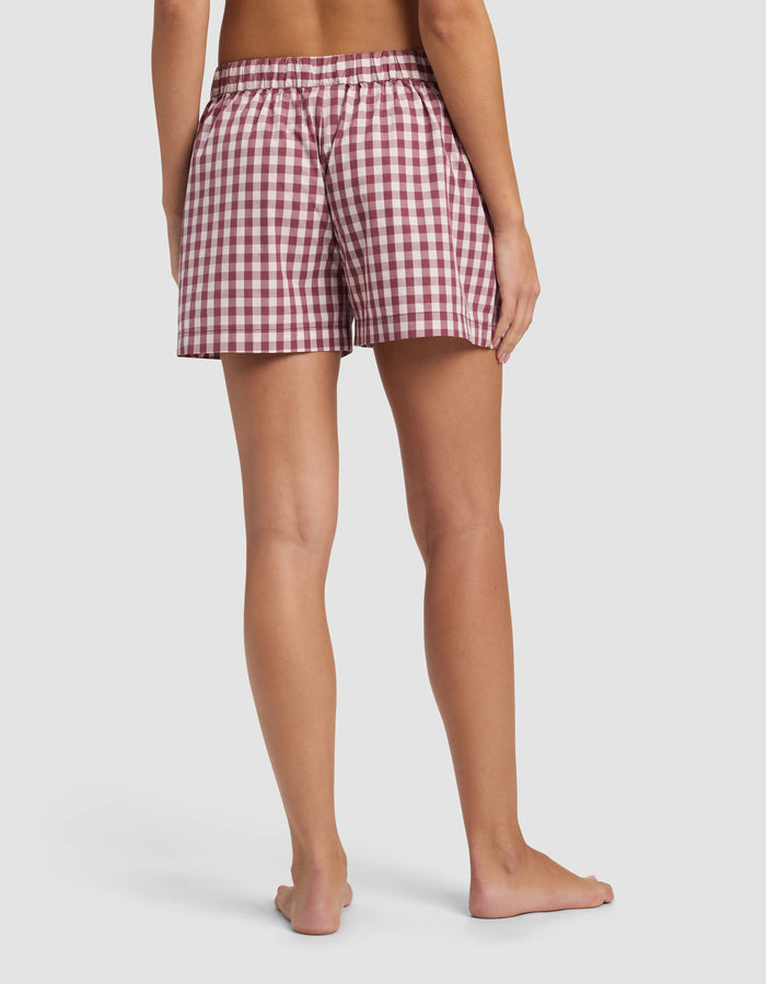 A person stands barefoot, facing away, wearing Cozy Earth's Women's Sutton Pajama Short in a red and white checkered pattern with an elastic waistband, against a plain white background.|Color:Mulberry Gingham