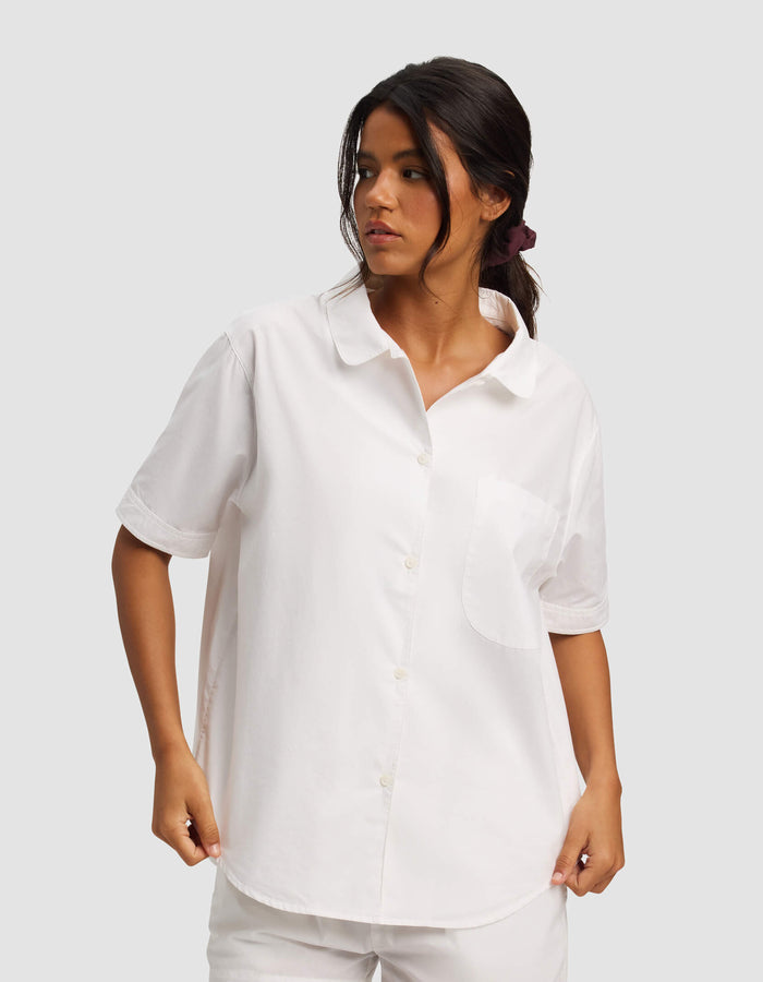 A woman stands against a plain light gray background wearing the Cozy Earth Women's Sutton Short Sleeve Pajama Top in white, paired with matching white shorts.|Color:White