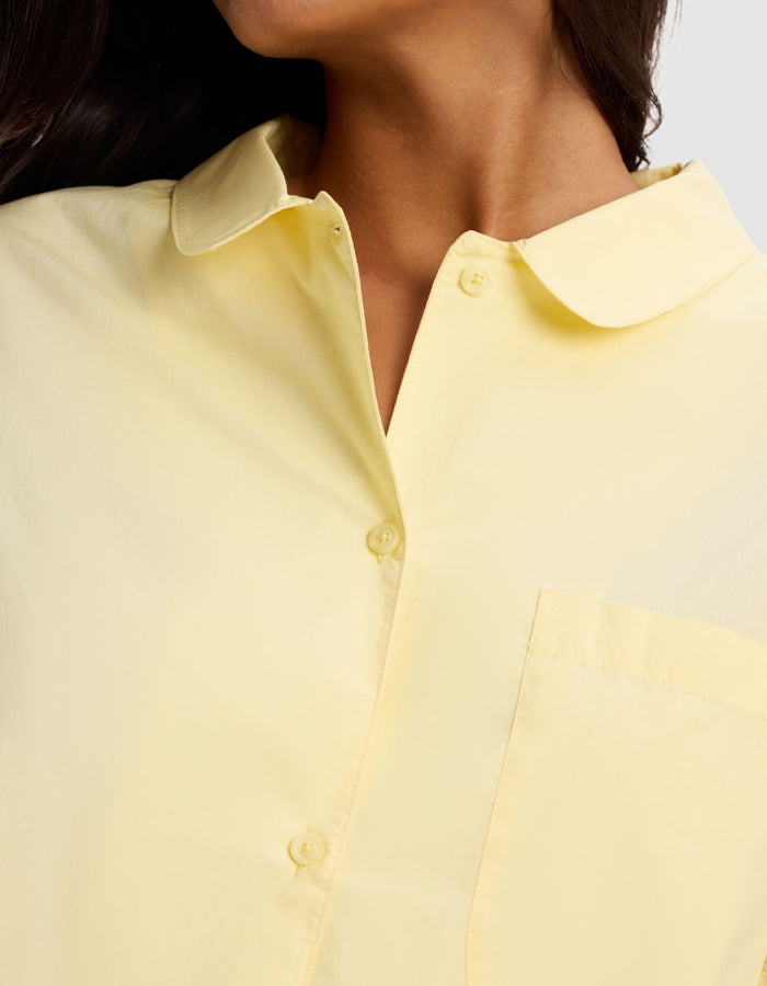 Close-up of a person wearing the Cozy Earth Women's Sutton Short Sleeve Pajama Top in pale yellow, featuring a collar and front pocket; focus is on the upper torso and neck with head partially visible, turned to the side.|Color:Meringue
