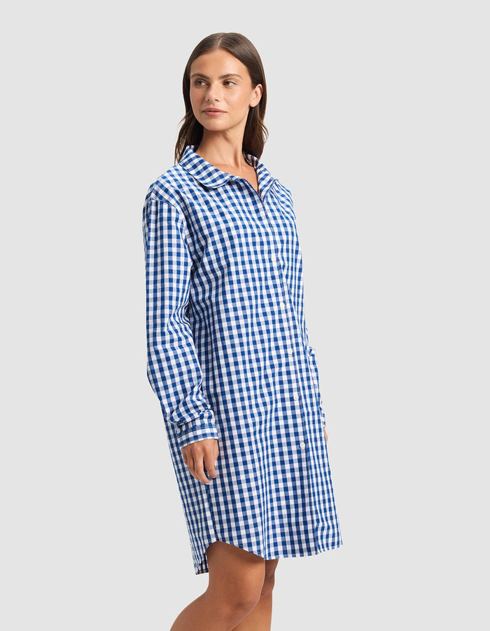 A woman wears the Cozy Earth Women's Sutton Sleep Dress, a blue and white checkered long-sleeve style, standing slightly left against a plain light gray background.|Color:Pacific Gingham