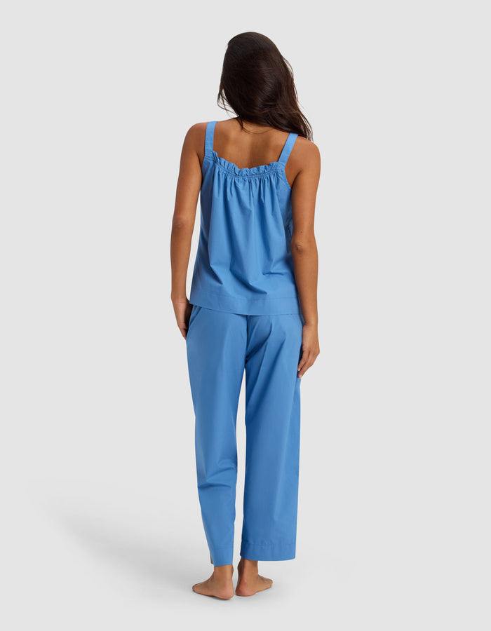 A woman stands barefoot facing away, wearing the Cozy Earth Women's Sutton Tank & Cropped Pant Pajama Set in blue against a plain, light background.|Color:Sailor