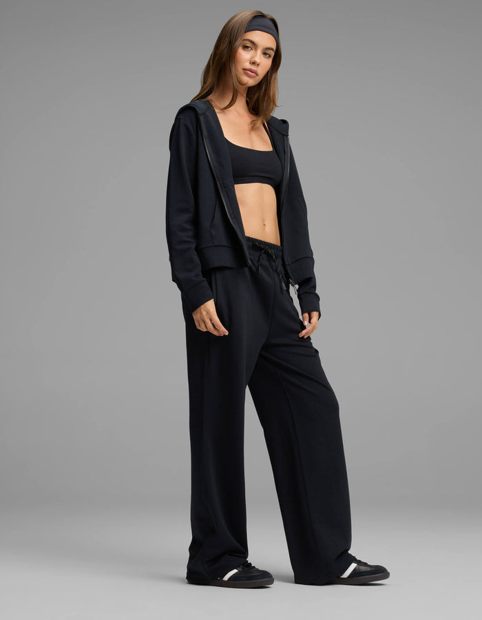 A woman stands confidently against a plain gray background, wearing the Cozy Earth Women's Versa Zip-Down Hoodie & Straight Leg Pant Set in black.|Color:Jet Black