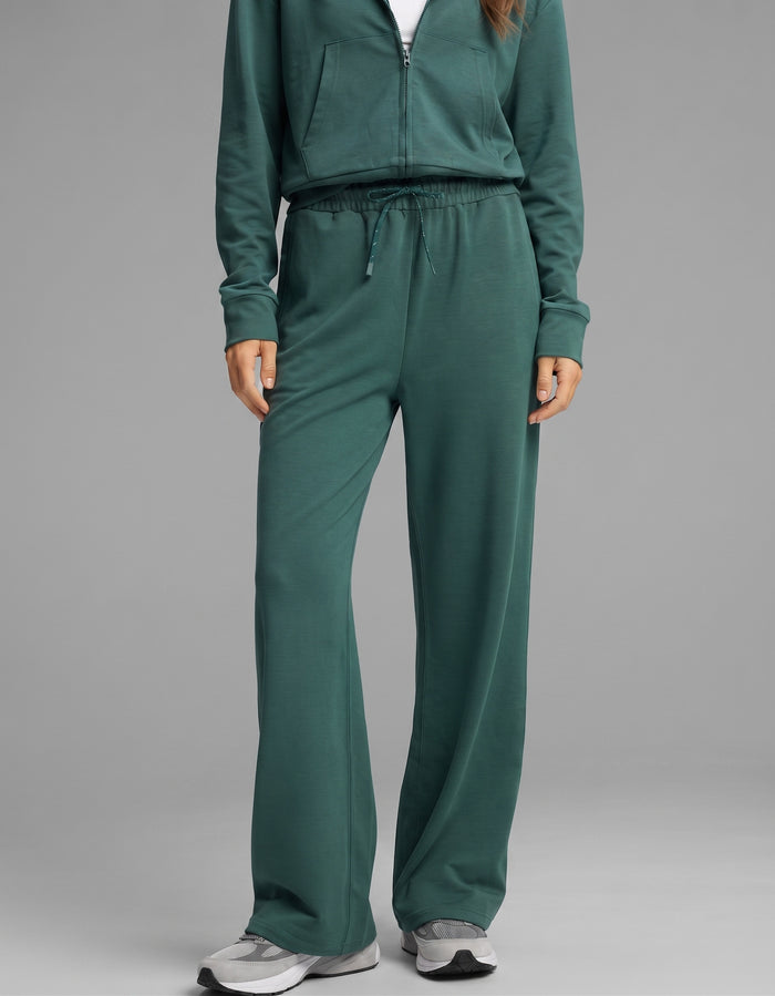A person wearing the Cozy Earth Women's Versa Zip-Down Hoodie & Straight Leg Pant Set in green with gray sneakers, standing against a neutral background. The person’s face is not visible.|Color:Uniform